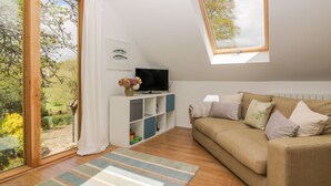 Un salón acogedor con sofá, televisor y vista a un jardín a través de un amplio ventanal.