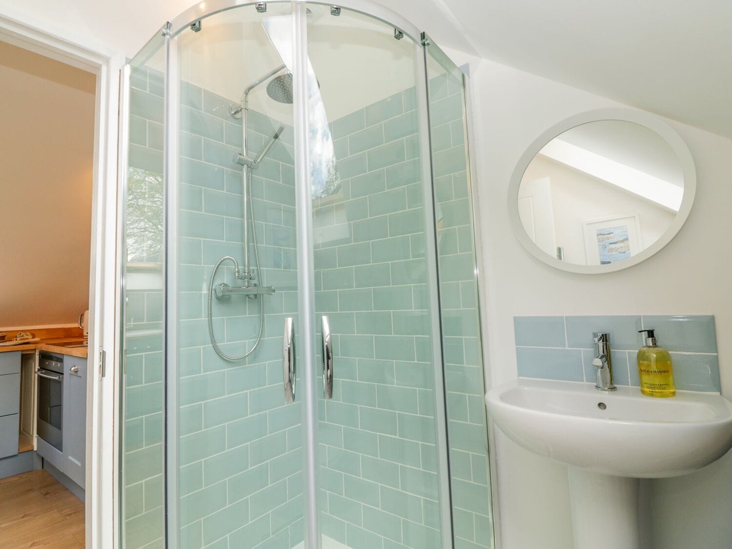 A bathroom with a glass-enclosed shower, a sink with a mirror, and light blue tiles.