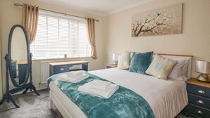 A bedroom with a bed, bedside tables, a dresser, a mirror, and a window with curtains. - Dune Haven (Truro)