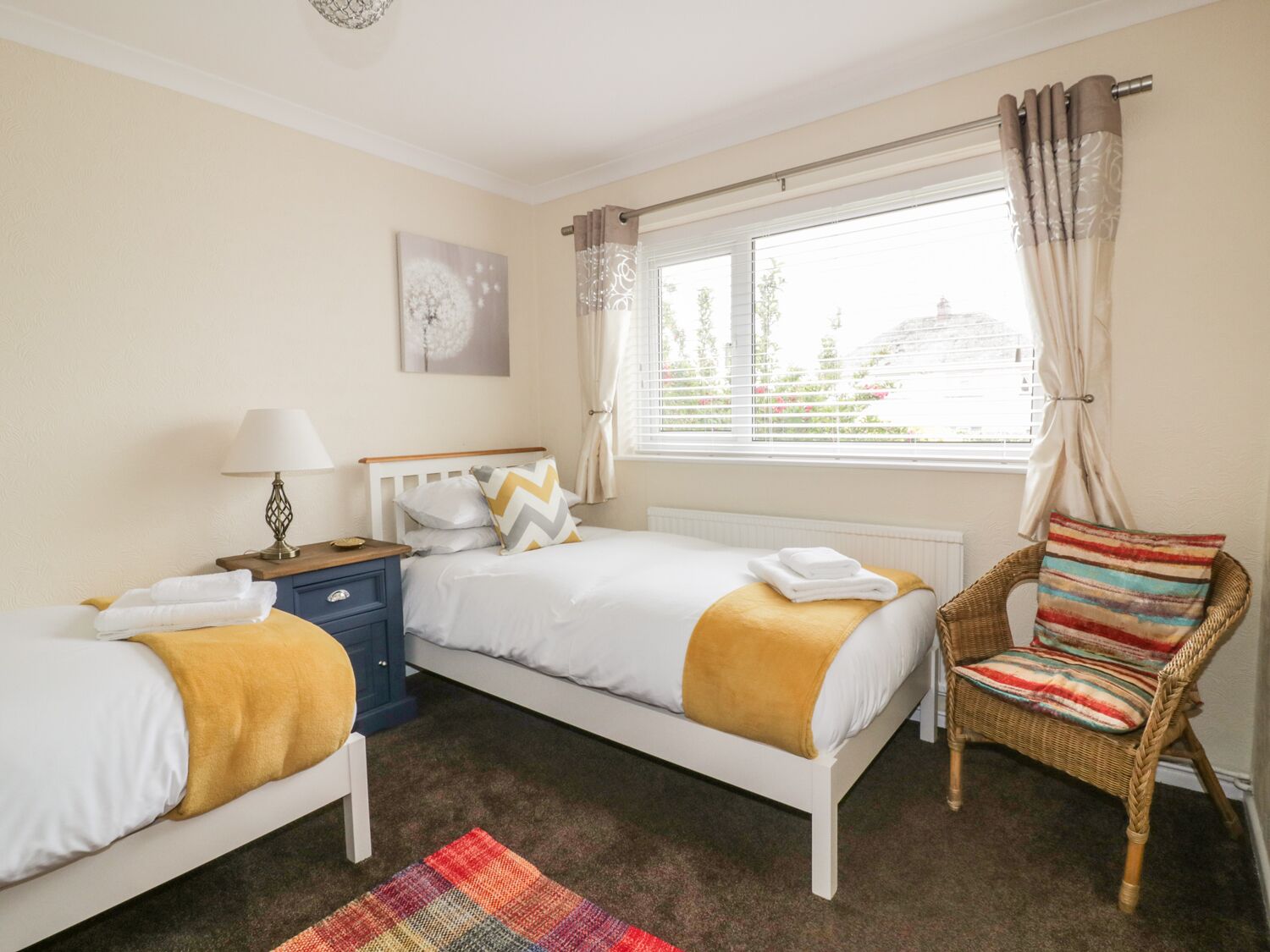 A bedroom with two beds, a nightstand, a lamp, a chair, and a window with curtains.