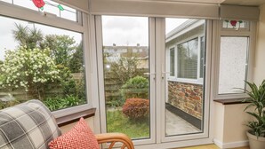 A cozy room with a sofa, a red patterned pillow, and a view of a garden through a glass door. - Dune Haven (Truro)