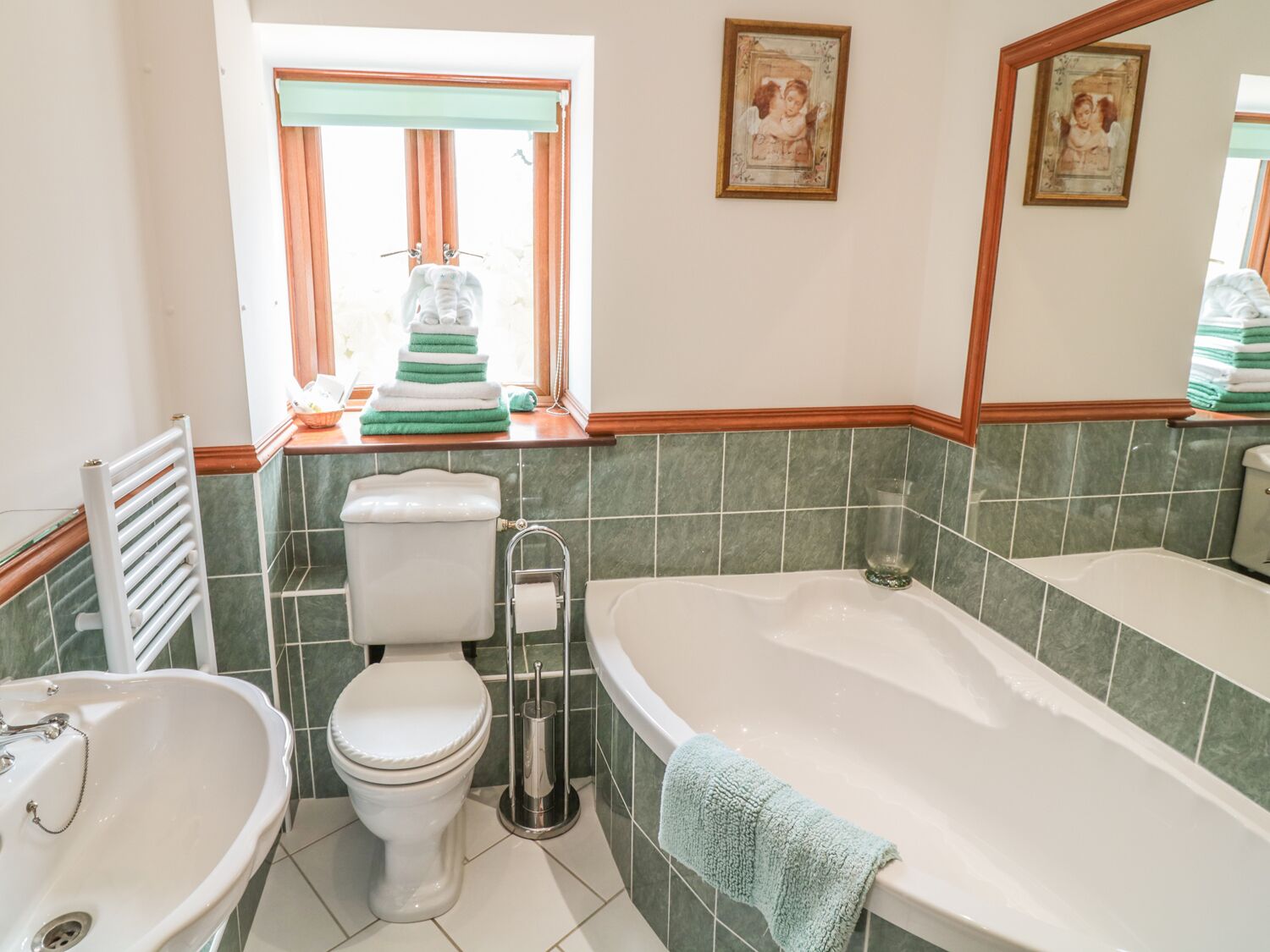 A bathroom with a toilet, sink, and bathtub. There are towels stacked on the windowsill, and two framed pictures on the wall.