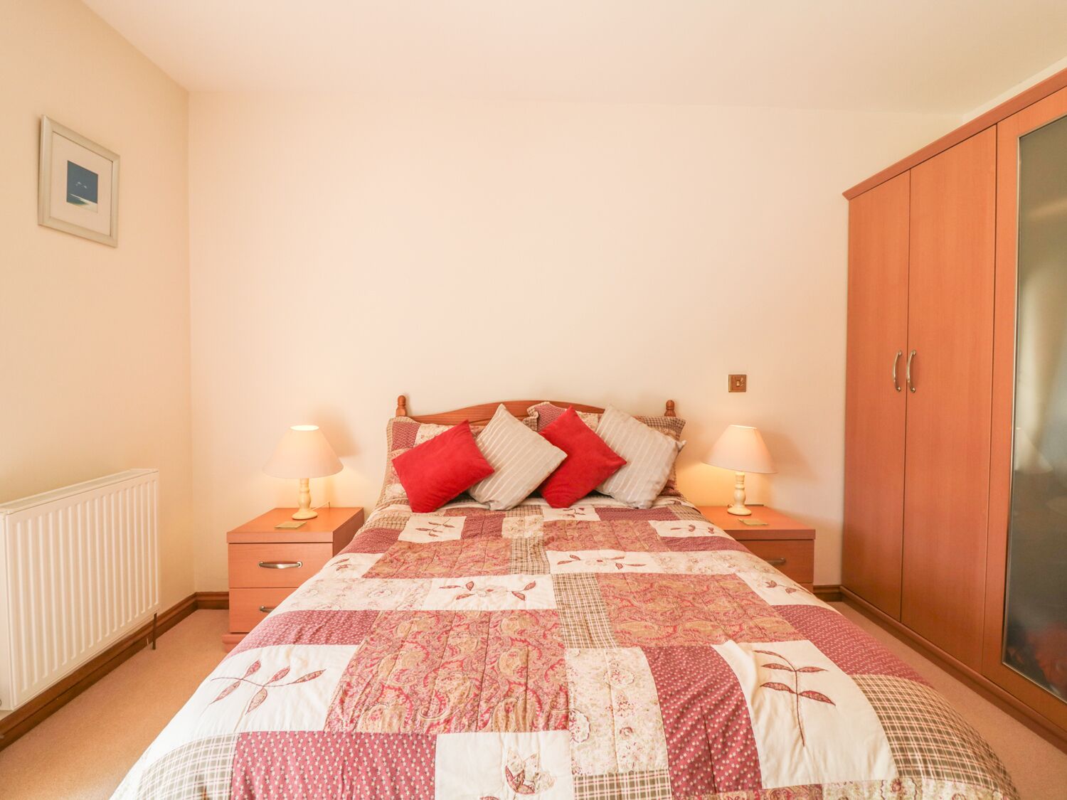Une chambre à coucher avec un lit en bois, deux tables de chevet avec des lampes, un radiateur et une armoire.