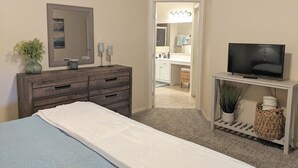 Een slaapkamer met een bed, een kaptafel, een televisie en een zichtbare badkamer door een geopende deur.