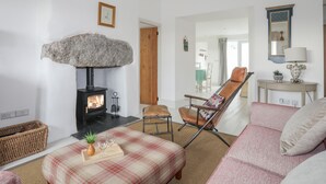 Ein gemütliches Wohnzimmer mit Kamin aus Stein, einer bequemen Couch, einem Sessel und einem Essbereich, der durch eine offene Tür sichtbar ist.