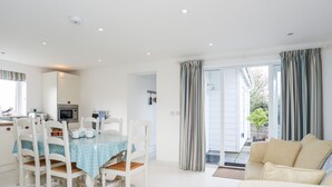 Ein helles, geräumiges Wohnzimmer mit Essbereich, einer Küche und einer Glastür, die auf einen Balkon führt.