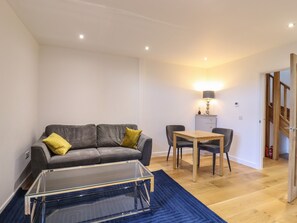 A modern living room with a grey sofa, a glass coffee table, and a wooden dining table with chairs.