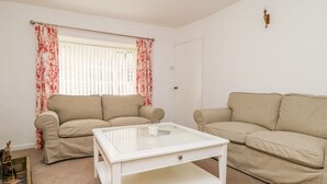 A living room with two beige sofas, a white coffee table, and a window with red floral curtains. - 11 Tower Street (Richmond)