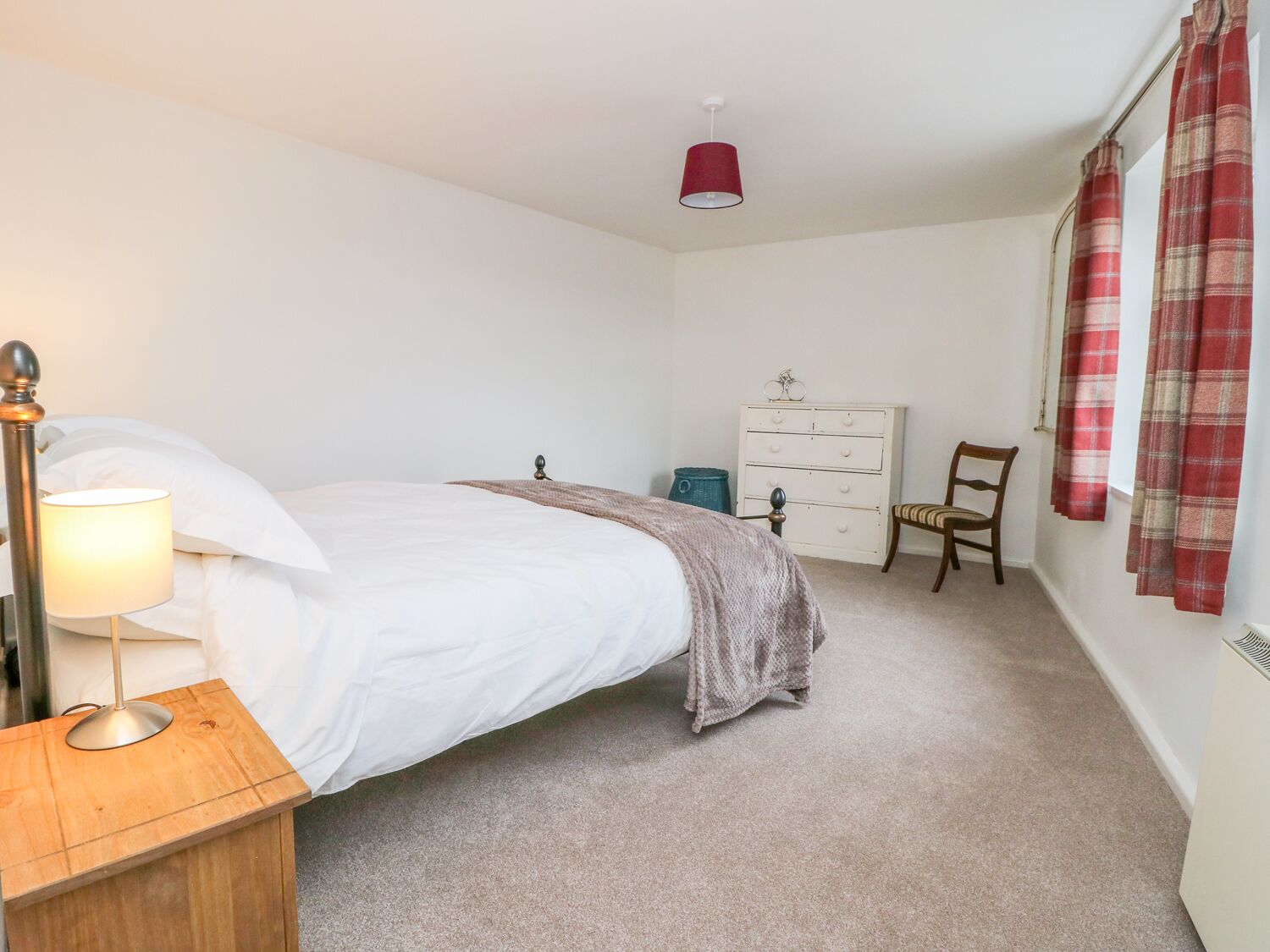 A bedroom with a bed, a nightstand, a dresser, a chair, and a red lamp.