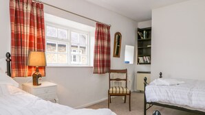 A bedroom with two beds, a nightstand with a lamp, a chair, a bookshelf, and a window with curtains. - 11 Tower Street (Richmond)