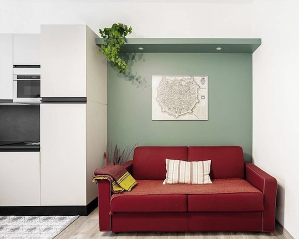 A compact living space with a kitchenette, a red sofa, a map artwork, and a green plant.