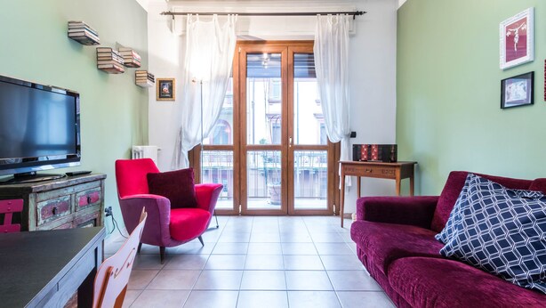 A living room with a television, a red chair, a red sofa, and a small table. - JOIVY Cozy Flat for 4 w/ Patio, Nearby Navigli (Milan)