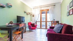 A living room with a television, a red armchair, a purple sofa, and a dining area with a table and chairs. - JOIVY Cozy Flat for 4 w/ Patio, Nearby Navigli (Milan)
