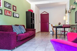 Un salon avec un canapé rouge, un fauteuil violet, une table à manger avec des chaises et une porte rouge.