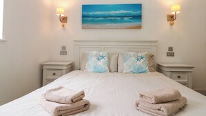 A neatly made bed with two pillows, two bedside tables, and a painting of a beach scene. - Sea Breeze (Filey)