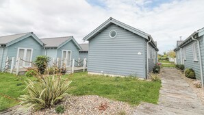 A row of light blue cottages with a grassy yard and a wooden pathway. - Sea Breeze (Filey)