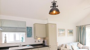 A kitchen with a dining area, a white cabinet, a sink, and a hanging light fixture. - Sea Breeze (Filey)