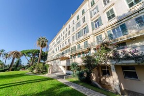 A multi-story building with a central staircase, balconies, and a well-maintained garden with palm trees. - JOIVY Lovely Apt with Communal Pool in Nervi (Genoa)