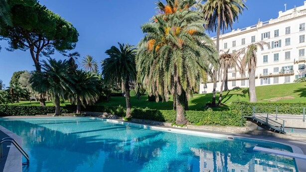 Une piscine à l’eau d’un bleu cristallin, entourée de palmiers et bordée d’une pelouse bien entretenue.