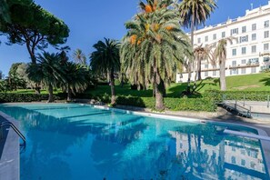 A swimming pool with clear blue water, surrounded by palm trees and a well-maintained lawn.