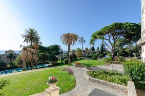 A landscaped garden with a pool, palm trees, and a pathway leading to a building. - JOIVY Lovely Apt with Communal Pool in Nervi (Genoa)