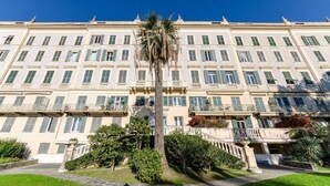 Un grand immeuble à plusieurs étages, doté d’une façade symétrique, de balcons et d’un palmier au centre.