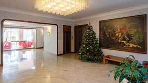 Un hall d’entrée spacieux, agrémenté d’un grand lustre, d’un sapin de Noël décoré et d’un tableau classique accroché au mur.