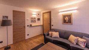 A modern living room with a grey sofa, wooden flooring, and a wooden door.