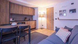 A compact living space with a kitchenette, a dining area, and a seating area with a sofa and a lamp.
