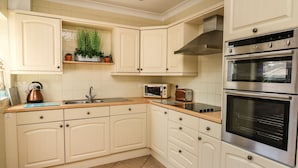 Una cocina con armarios blancos, horno de acero inoxidable, microondas y hervidor en la encimera.