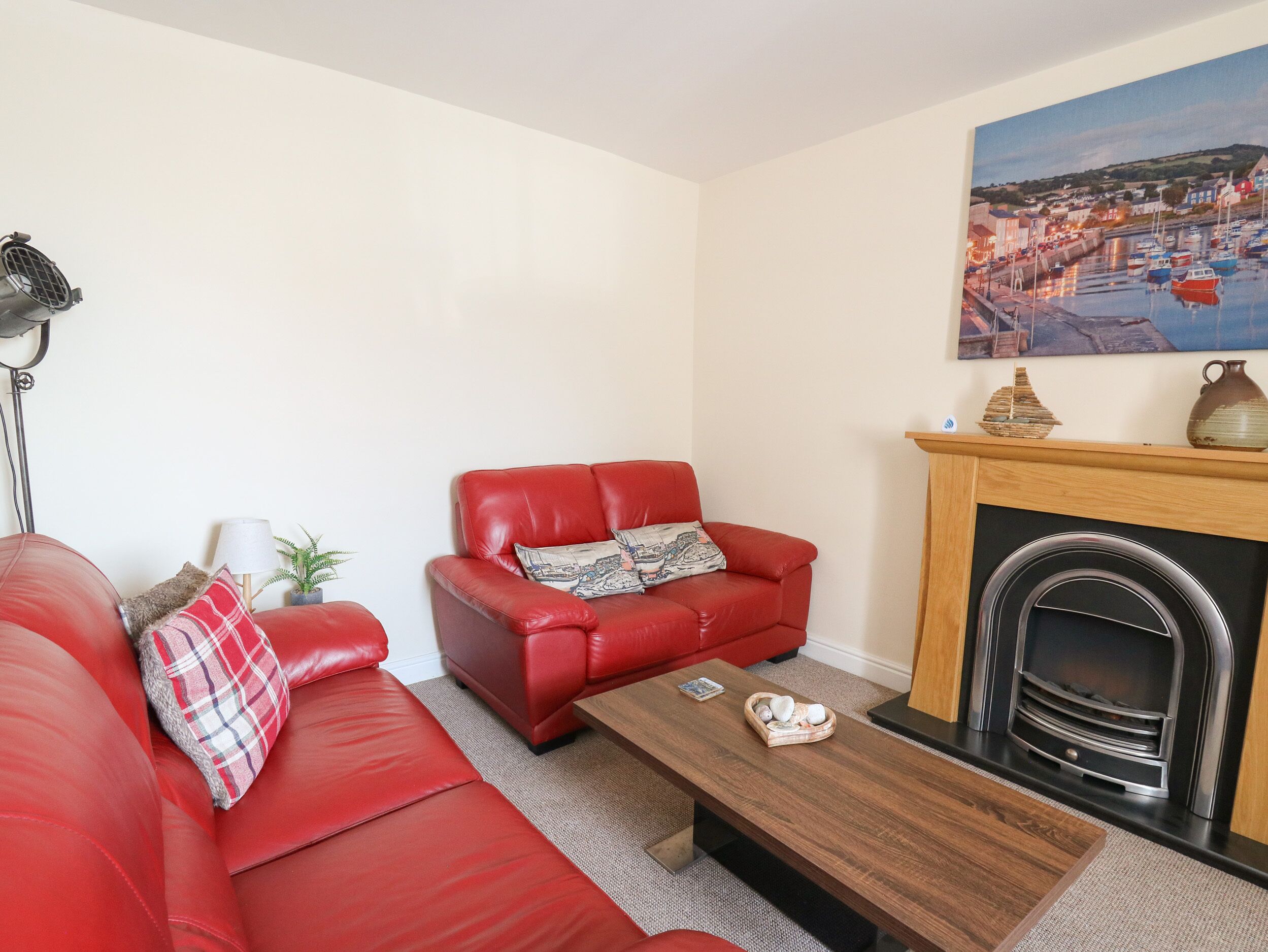A living room with a red sofa, a wooden coffee table, a fireplace, and a painting of a coastal scene.