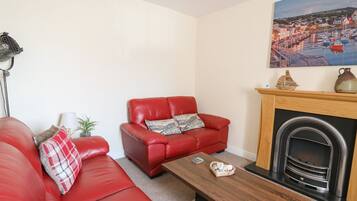 A living room with a red sofa, a wooden coffee table, a fireplace, and a painting of a coastal scene.