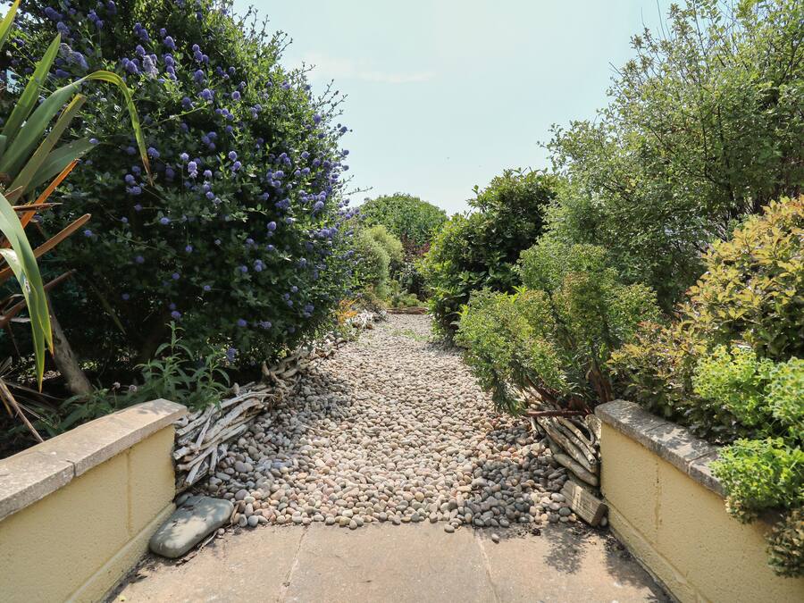 A pathway lined with pebbles and surrounded by lush greenery and flowering bushes.