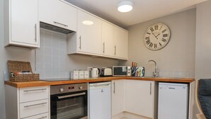 Una cocina compacta con armarios blancos, horno integrado, microondas, lavavajillas y un reloj de pared.