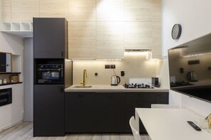 Uma cozinha moderna com forno embutido, fogão a gás, pia com torneira dourada e um relógio na parede.