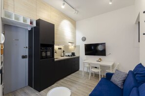 Um apartamento moderno com cozinha compacta, área de refeições, sala de estar com sofá azul e televisão de tela plana na parede.