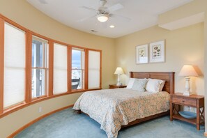 A bedroom with a bed, two bedside lamps, a nightstand, a ceiling fan, and a window with blinds. - Home On The Range: Private Pool, Hot Tub, Elevator, Village Beach Club Access (Nags Head)