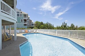 A swimming pool with lounge chairs, a white fence, and multi-story buildings in the background. - Home On The Range: Private Pool, Hot Tub, Elevator, Village Beach Club Access (Nags Head)