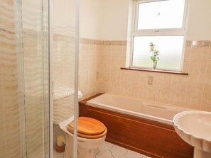 A bathroom with a glass shower enclosure, a wooden toilet, a bathtub, and a window with a view of greenery. - Cleary Cottage (Miltown Malbay)