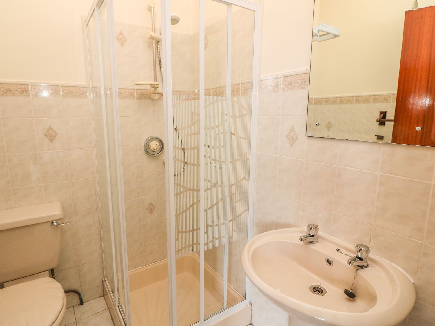 A bathroom with a glass-enclosed shower, a toilet, and a sink with a mirror above it.