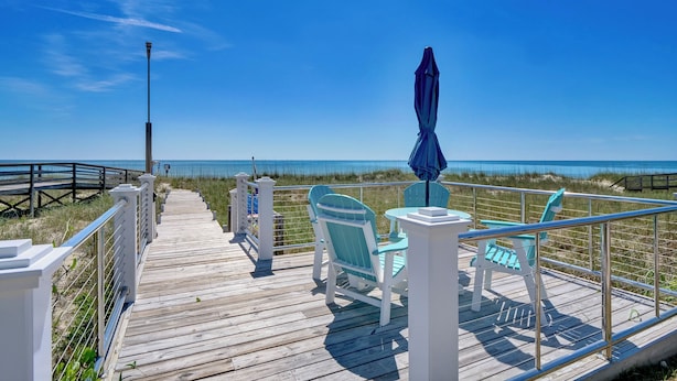A wooden deck with chairs and a table, overlooking a beach with a clear view of the ocean. -  Siren's Song--Gorgeous Oceanfront House with Pool and Spa! (Kure Beach)