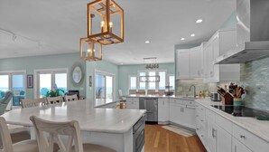 A modern kitchen with white cabinets, a large island, and a view of the ocean. -  Siren's Song--Gorgeous Oceanfront House with Pool and Spa! (Kure Beach)