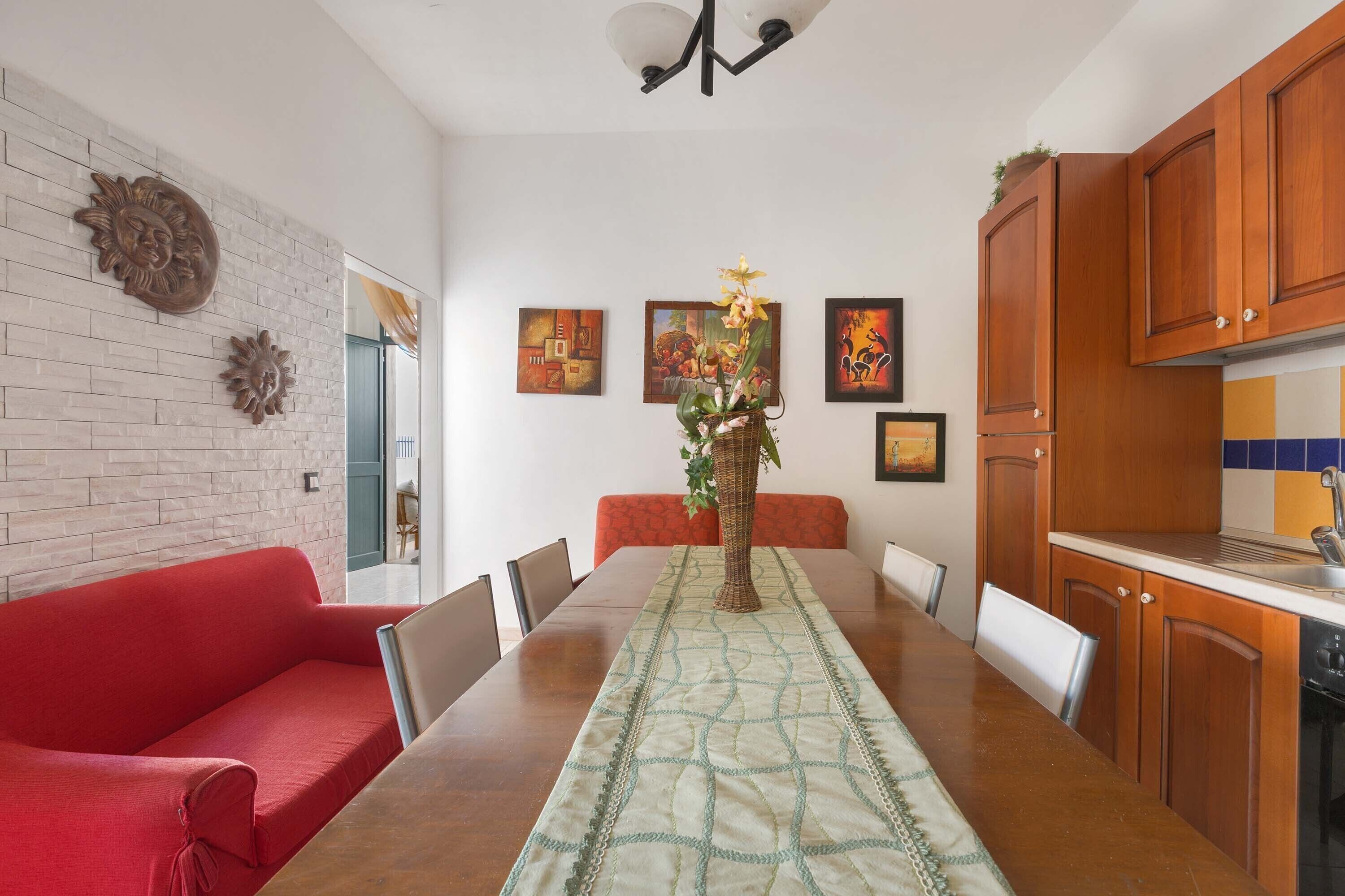 A dining area with a long table, red sofa, and wooden cabinets.