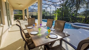 Un área de comedor al aire libre cubierta con vista a la piscina, con una mesa para cuatro sillas y una barandilla de vidrio alrededor del espacio.