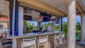 Un área de bar al aire libre con mostrador, taburetes y vistas de la vegetación circundante.
