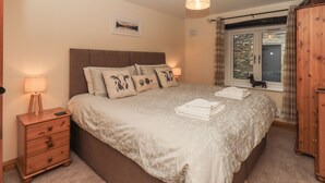 Een slaapkamer met een bed, nachtkastjes, een lamp, een raam met gordijnen en een houten kledingkast.