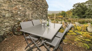 Een stenen muur, een metalen tafel met stoelen en een fles wijn.