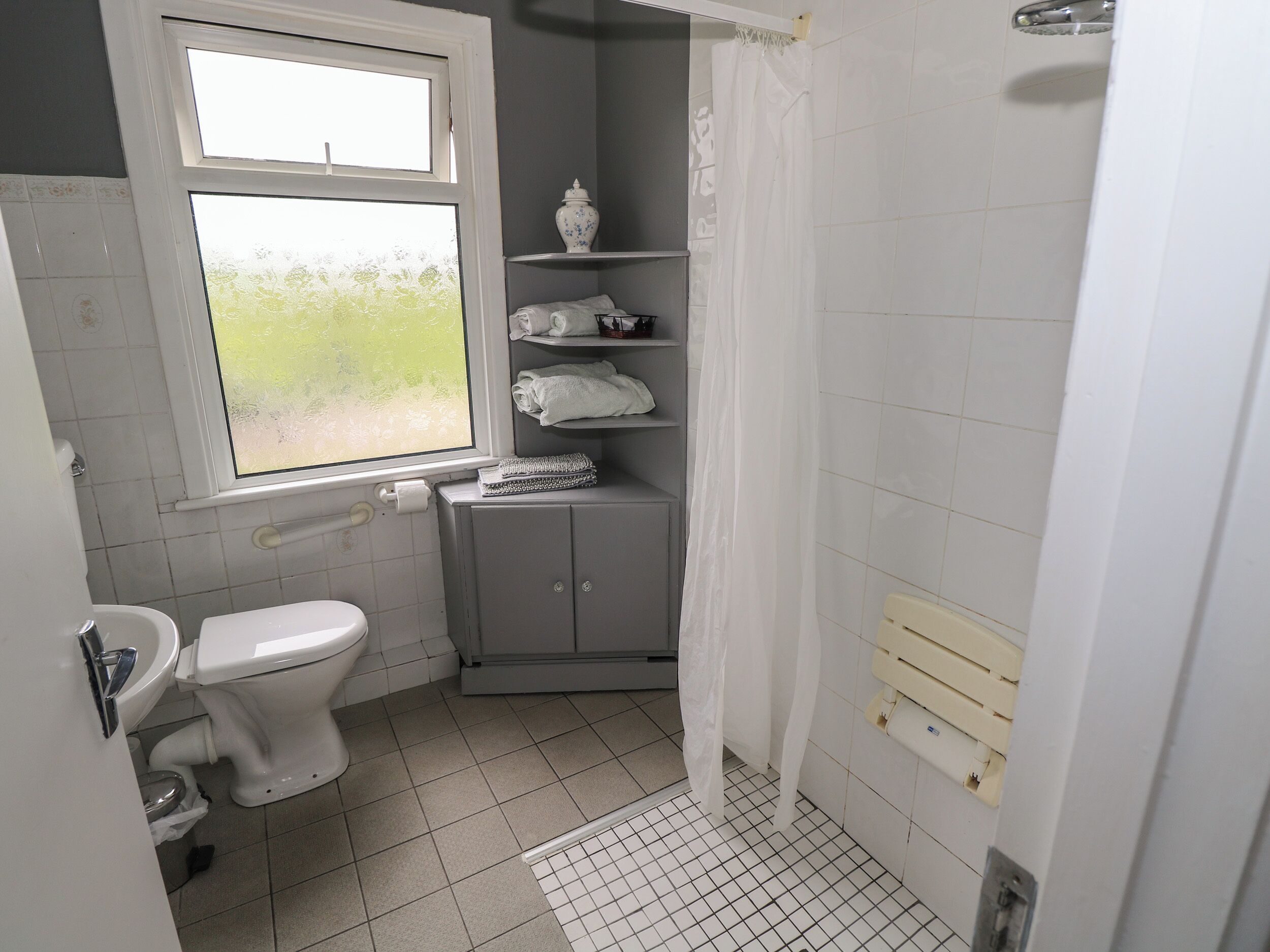 Ein kleines, kompaktes Badezimmer mit Toilette, Fenster, Dusche und Handtuchhalter.