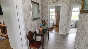 Un pasillo con suelo de madera, una silla, una mesa con un jarrón de flores y un espejo en la pared.