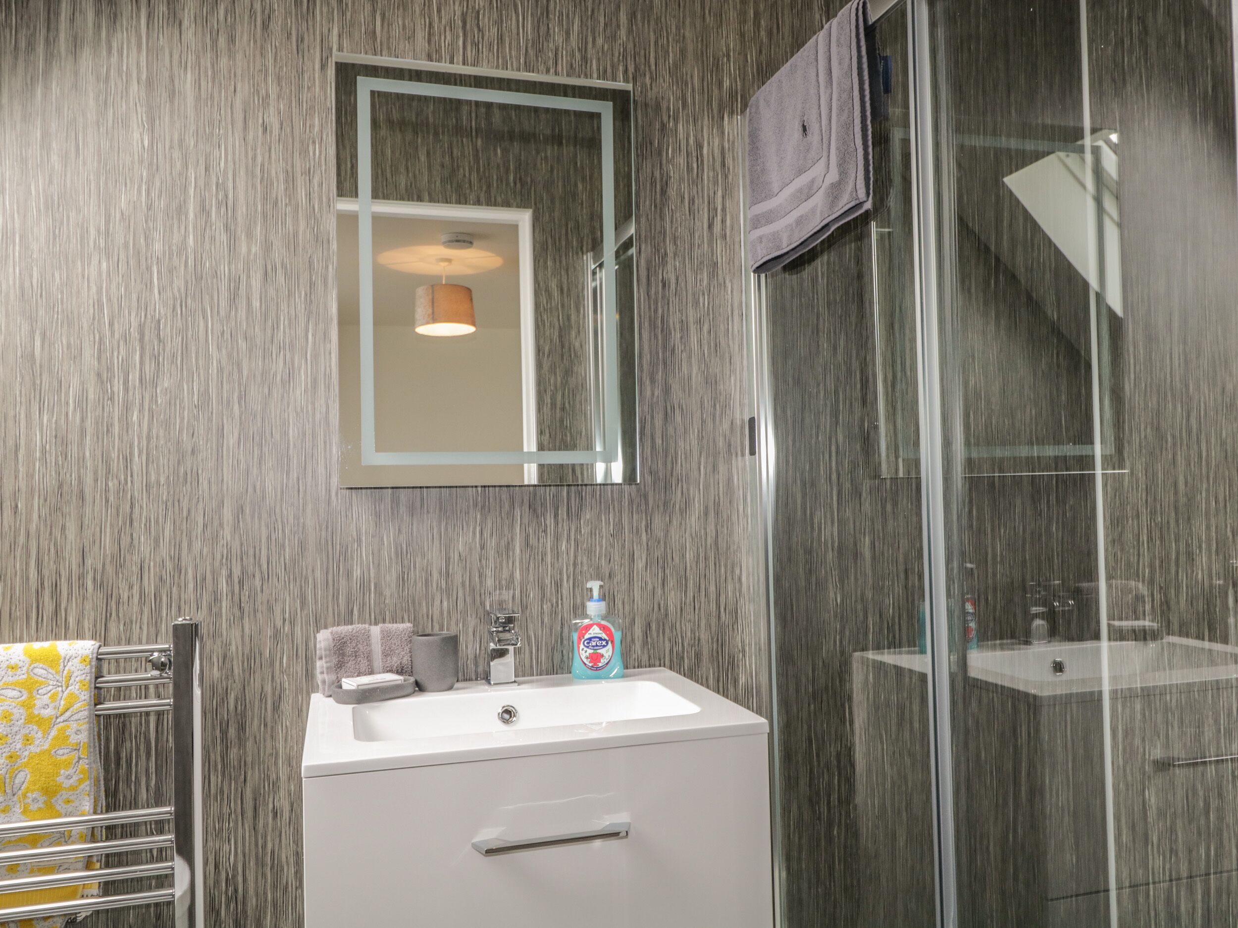 A modern bathroom with a large mirror, a sink, and a glass shower enclosure.